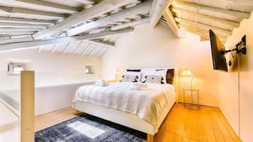 A bedroom with a sloped ceiling, a bed with a patterned bedspread, two bedside lamps, and a small round table.