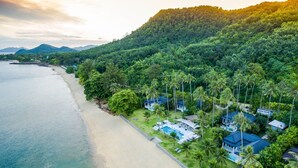 An aerial view of a coastal resort with beachfront villas, a swimming pool, and lush greenery.