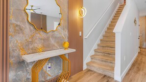 A modern interior with a marble wall, a wooden slatted wall, a white staircase, and a white console table with a globe and a candle.