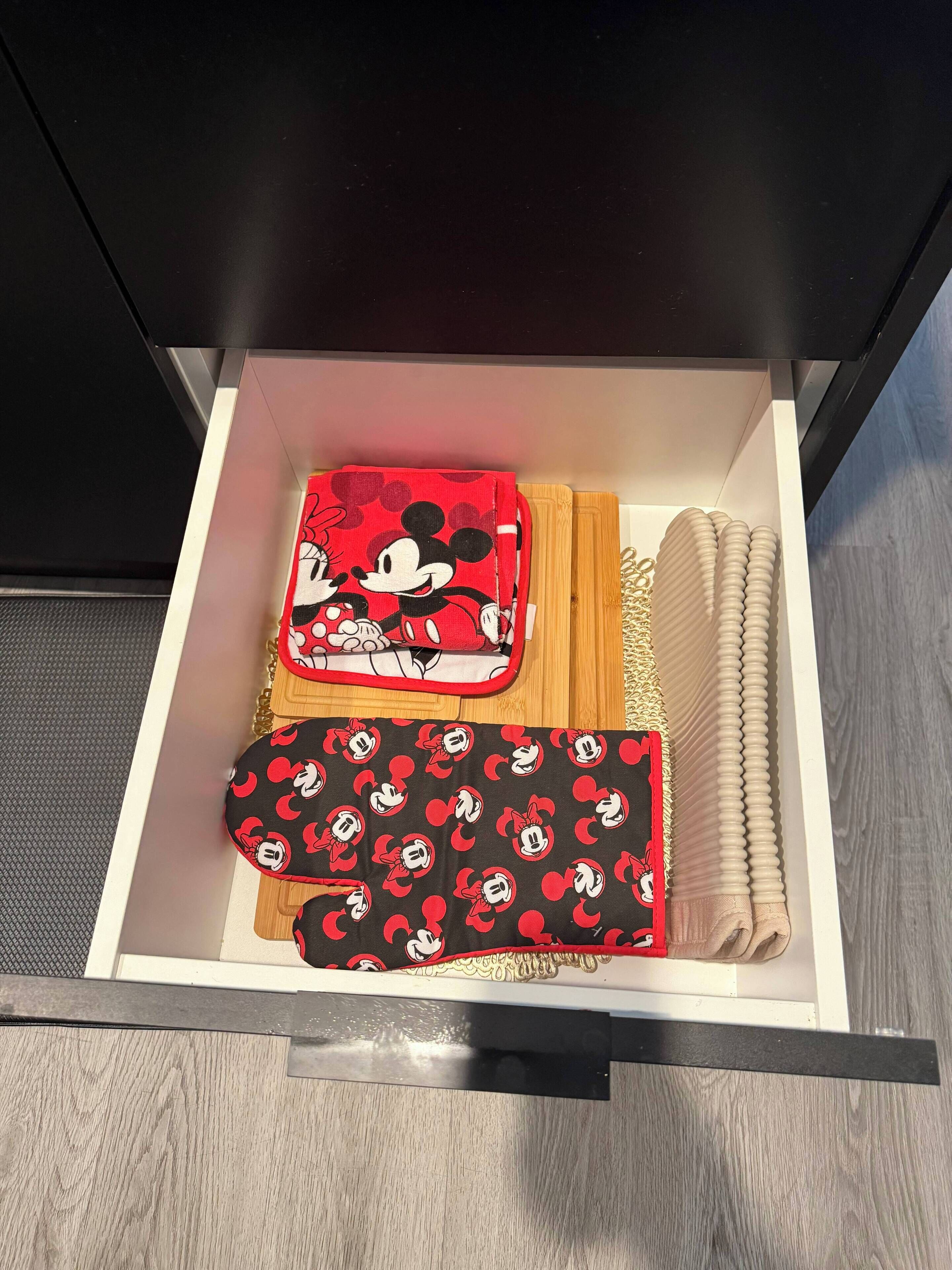 Un tiroir contenant des articles sur le thème de Mickey Mouse, notamment un sac rouge, un coussin noir et rouge à l’effigie de Mickey, et des cordes beiges enroulées.