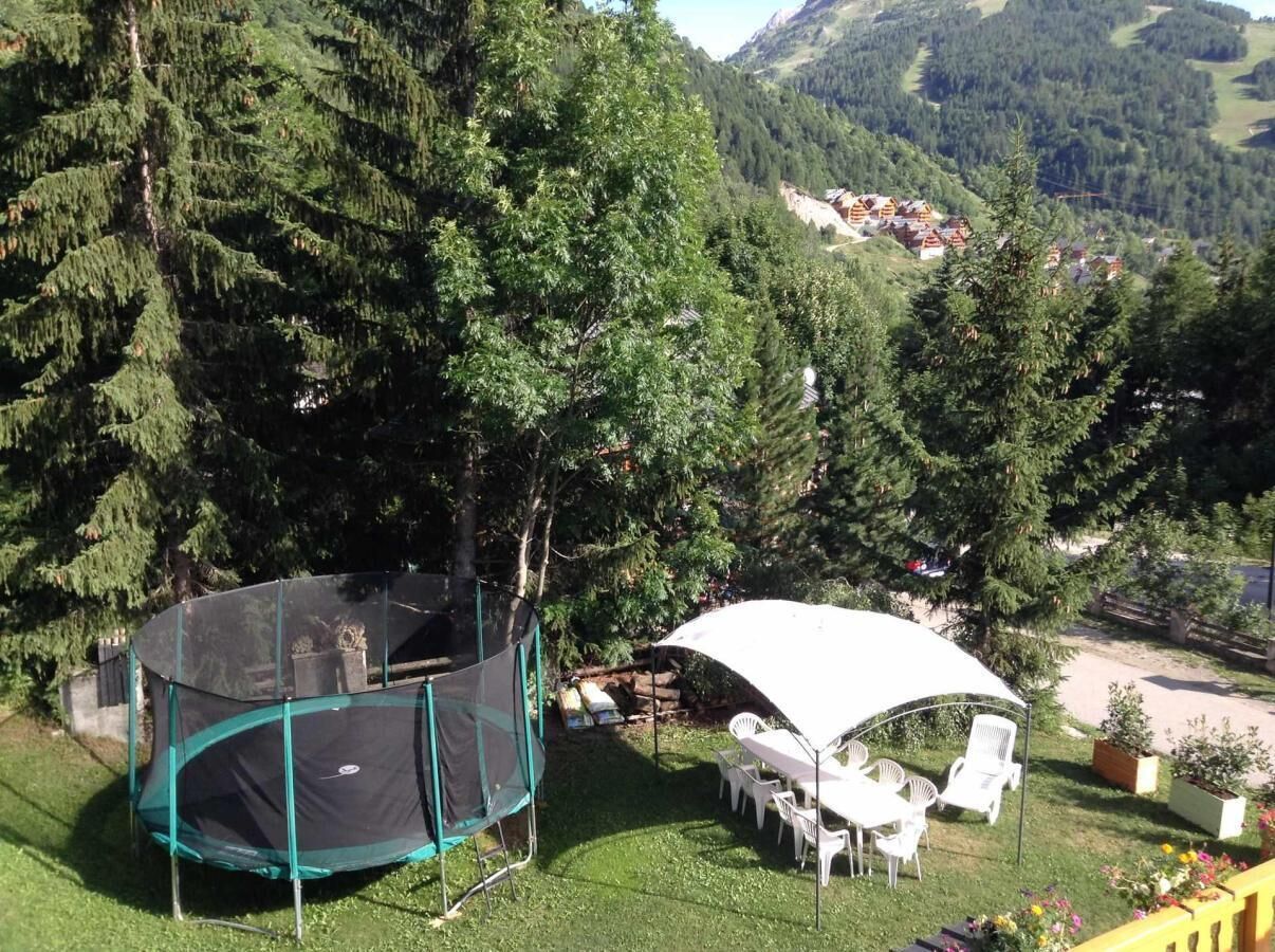 Un patio trasero con un trampolín, una zona de estar cubierta y vistas a un paisaje montañoso.