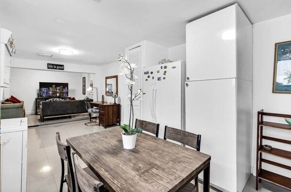 Une cuisine moderne avec des appareils électroménagers blancs, une table à manger avec des chaises, une plante en pot et un banc.