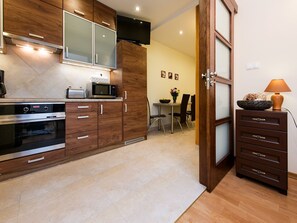 A modern kitchen with wooden cabinets, a microwave, and an oven. There is a dining area with a table and chairs visible through an open door.