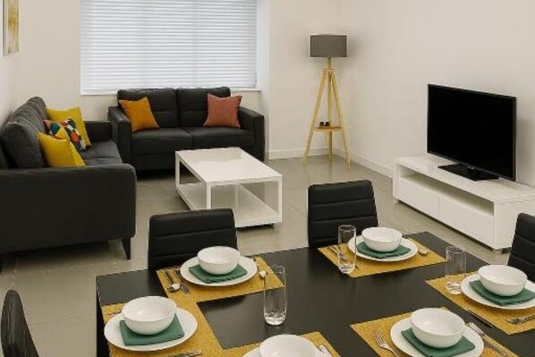 Un salon moderne comprenant un canapé, une table basse, une table à manger pour quatre personnes et un téléviseur.