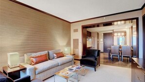 Un salon moderne avec un canapé, un fauteuil et une table basse. On aperçoit à l’arrière-plan un coin repas avec une table et des chaises.