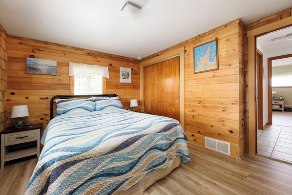 Un dormitorio con paneles de madera, una cama, mesitas de noche y un ventanal con cortinas.