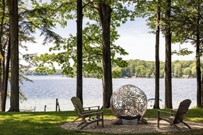 A lakeside view with two Adirondack chairs, a decorative sphere, and a bench. - Long Lake Stone Cottage in Traverse City Frontage  Kayaks Fire pit  Pet friendly (Traverse City)