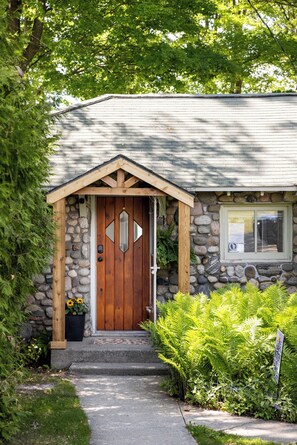 A stone house with a wooden door, a small porch, and a window. - Long Lake Stone Cottage in Traverse City Frontage  Kayaks Fire pit  Pet friendly (Traverse City)