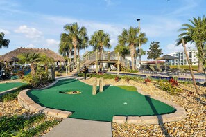Un parcours de minigolf doté d’un green, entouré de palmiers et surmonté d’un pont en bois.