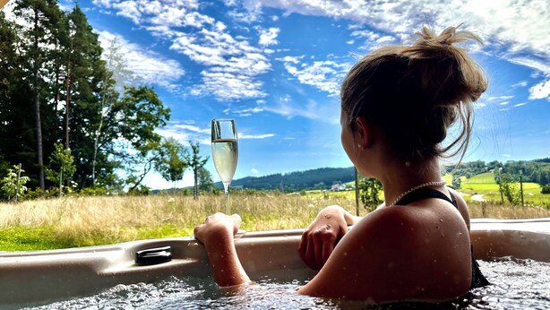 A person in a hot tub with a glass of champagne, surrounded by a scenic outdoor view. - Vacation home in a secluded location for relaxing and active vacations (Patersdorf)