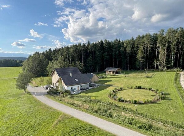 A rural house with a paved driveway, surrounded by a well-maintained lawn and a forested area. - Vacation home in a secluded location for relaxing and active vacations (Patersdorf)