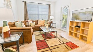 A living room with a brown sofa, a glass coffee table, a TV on a wooden stand, and a patterned rug.