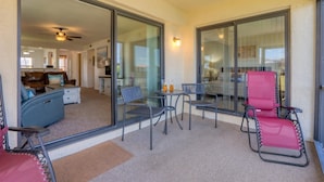 A balcony with a glass door, a dining table with chairs, and a red chair.