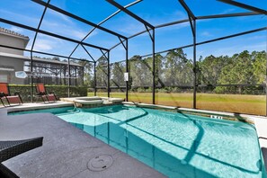 A covered outdoor swimming pool with a hot tub, lounge chairs, and a view of a building and trees. - BPD2920 Summary:<br>Para (Kissimmee)