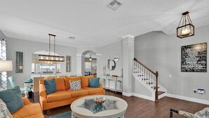 A spacious living room with a large orange sofa, a glass coffee table, and a staircase leading to another level. - TT7752 Summary:<br>Winds (Kissimmee)