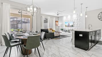 A modern kitchen with a central island, a dining area with a round table and chairs, and a living area with a sofa and TV.