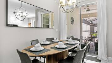 A dining area with a round table set for six, surrounded by black chairs. A large mirror hangs on the wall above the table, reflecting the room.