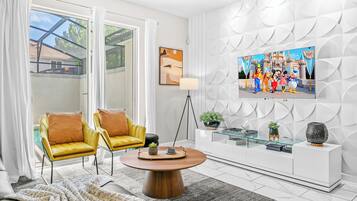 A modern living room with a glass coffee table, yellow chairs, a white entertainment unit, and a TV displaying Disney characters.