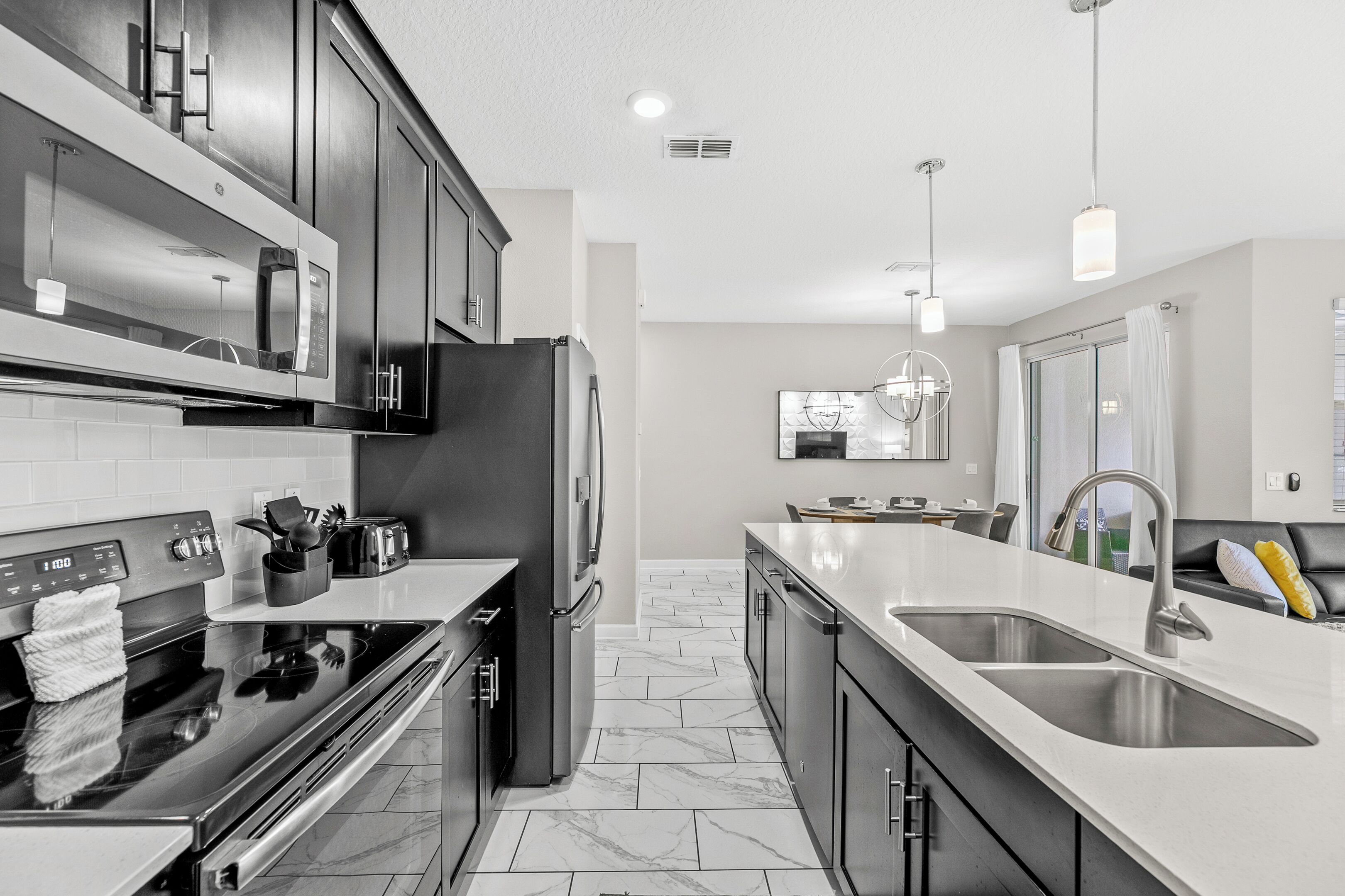 A modern kitchen with stainless steel appliances, a double sink, and a marble-tiled floor.