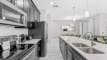 A modern kitchen with stainless steel appliances, a double sink, and a marble-tiled floor.