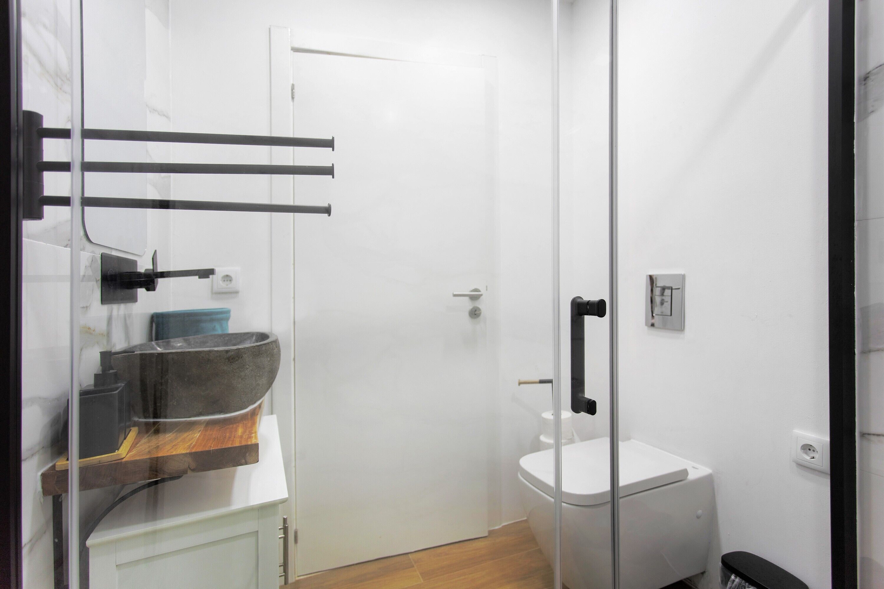 A modern bathroom with a glass shower enclosure, a white toilet, and a wooden vanity with a large sink.