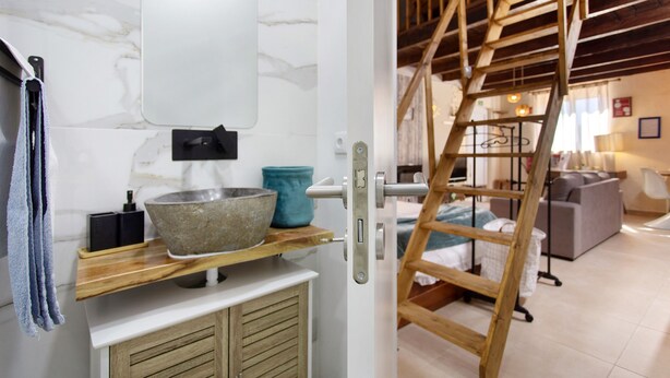 Un baño moderno con pared de mármol, escalera de madera y lavabo con pila de piedra.