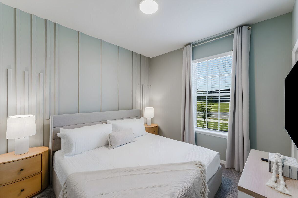 Une chambre d’hôtel avec un grand lit, deux tables de chevet avec des lampes, une fenêtre avec des rideaux et un téléviseur à écran plat.