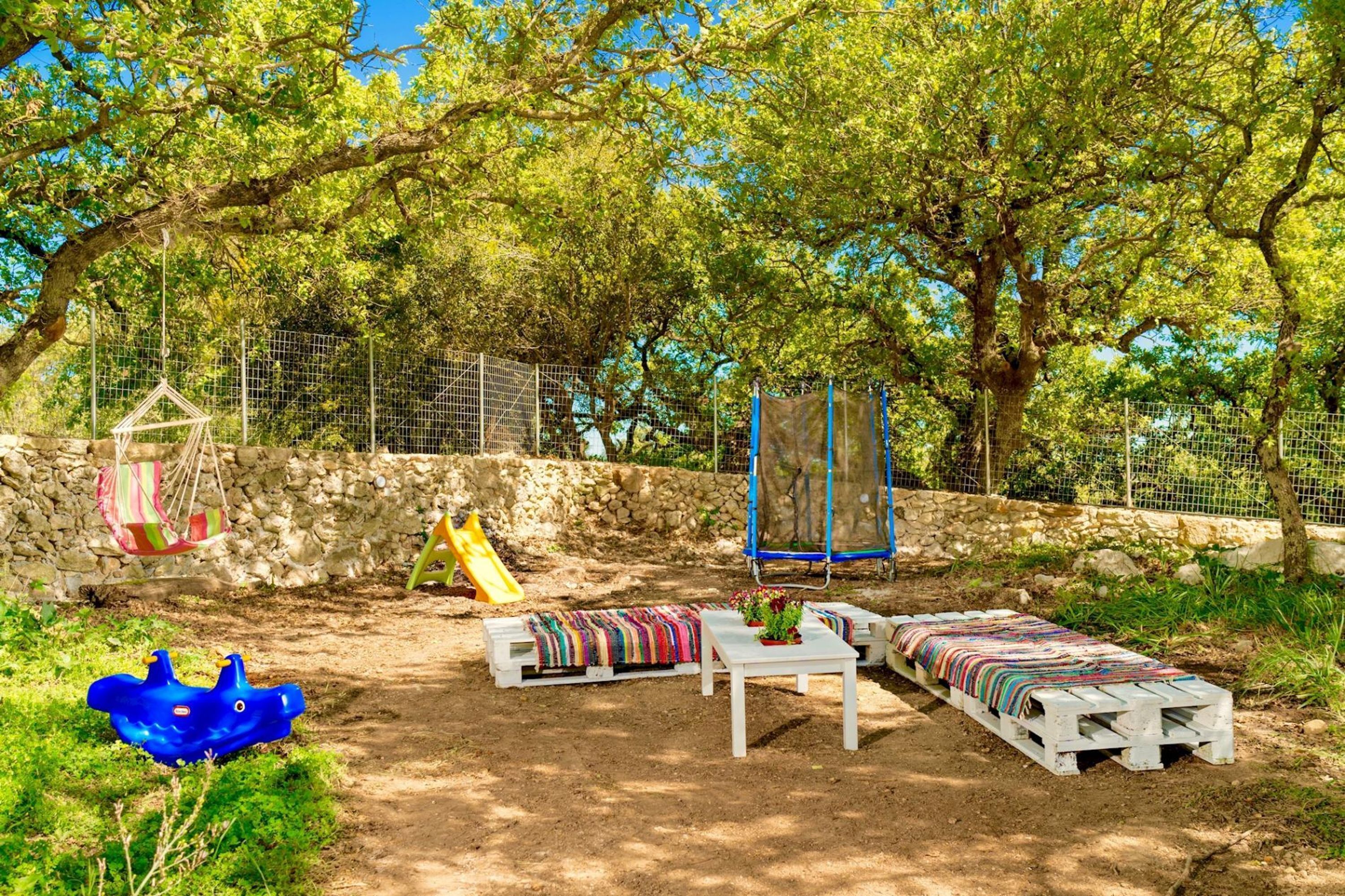 An outdoor seating area with a table and benches, surrounded by trees and a stone wall.