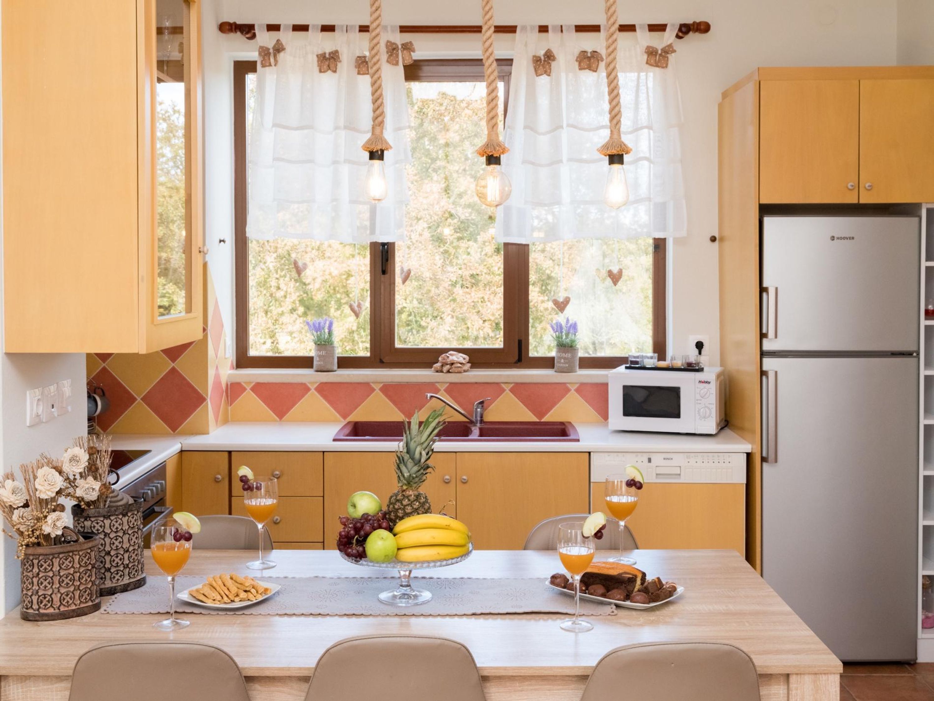 Une cuisine avec un coin repas, comprenant un panier de fruits, deux verres de jus d’orange et un four à micro-ondes.