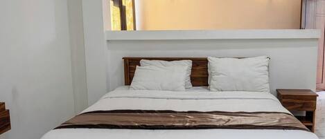 A neatly made bed with white linens, two bedside tables with wooden finishes, and two wall-mounted light fixtures.