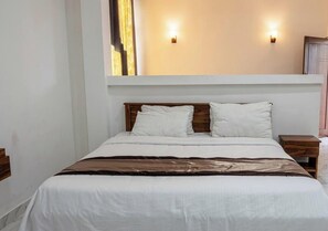 Een net opgemaakt bed met witte lakens, twee nachtkastjes met houten details en twee wandlampen.