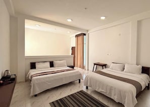 Habitación de hotel con dos camas, un ventanal con cortinas, una mesita y una mesita de noche.