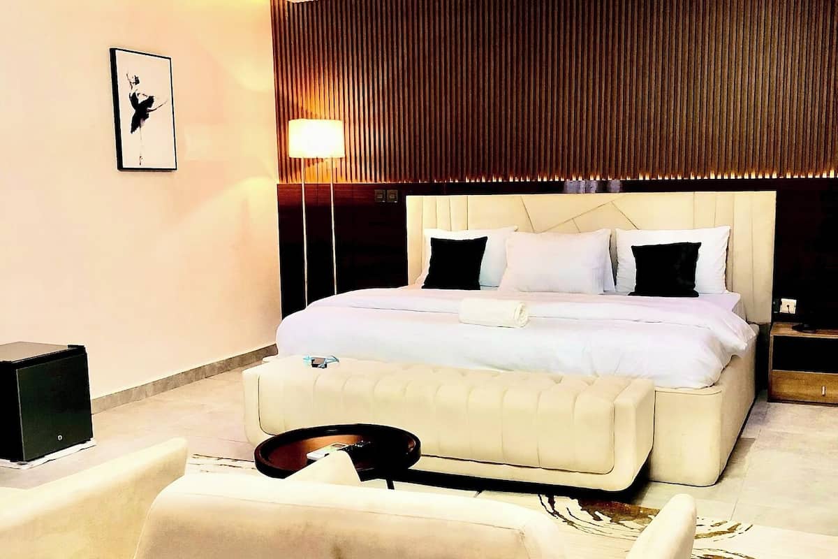 A modern hotel room with a large bed, a sofa, a flat-screen TV, and a wall-mounted lamp.