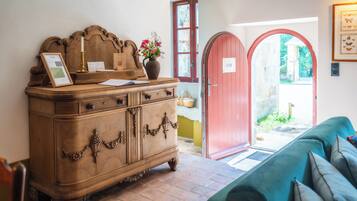 Un aparador de madera con un jarrón de flores, un cuadro enmarcado y una vela. Hay una puerta roja y un sofá verde en la habitación.