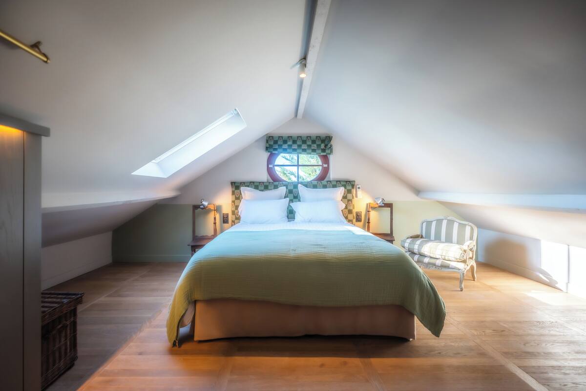 A bedroom with a large bed, a chair, and a skylight.