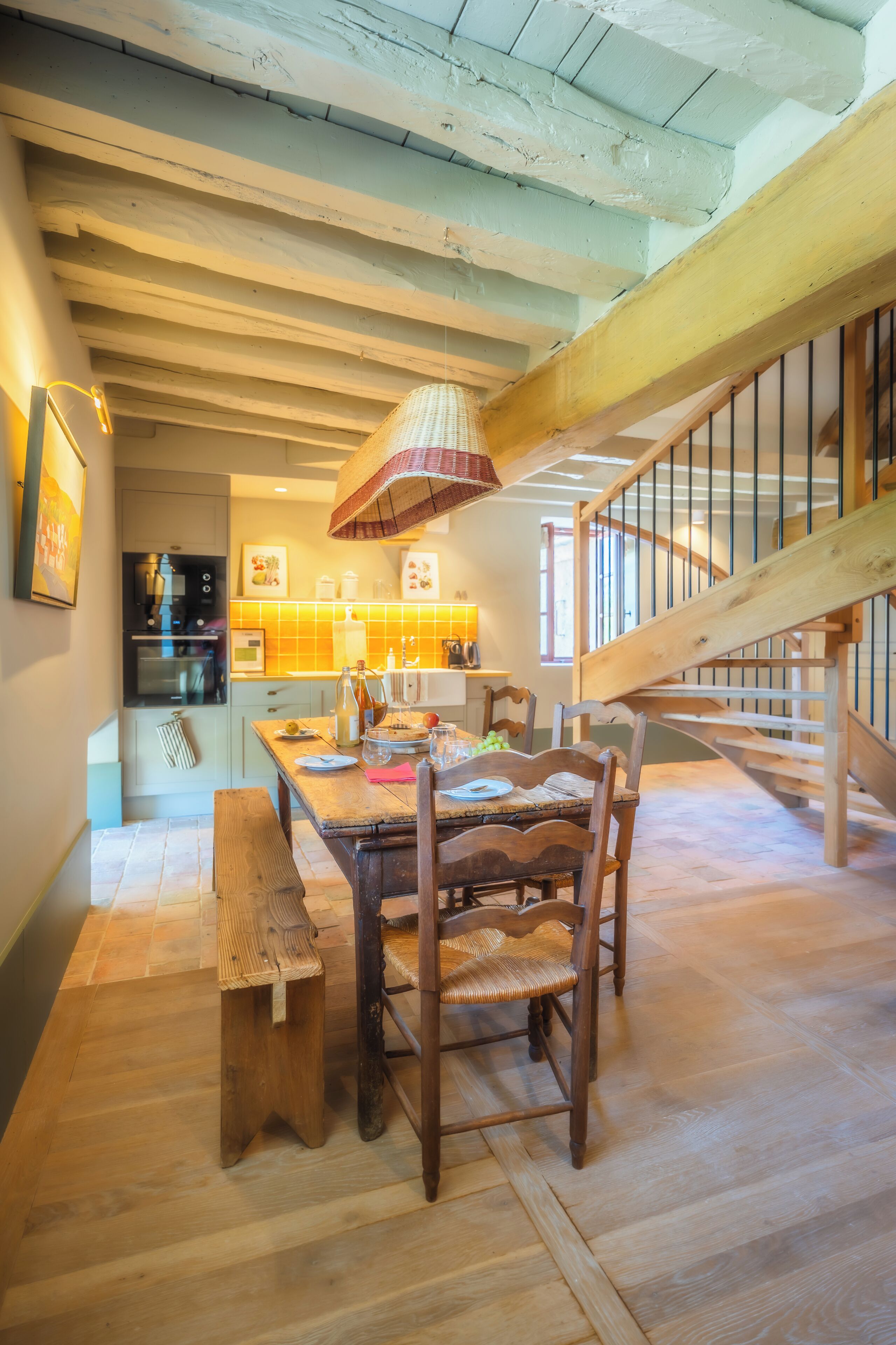 Una cocina rústica con vigas de madera, una mesa de comedor con sillas y una escalera con barandilla.
