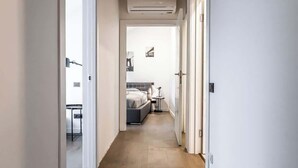 A narrow hallway with wooden flooring, white walls, and a ceiling with exposed beams. There are framed pictures on the wall and an air conditioning unit mounted on the wall. - Domillion cozy 3bdr apt in oldtown P364b (Vilnius)