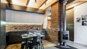 A modern kitchen with a brick accent wall, a dining table with chairs, and a wood-burning stove. - Domillion cozy 3bdr apt in oldtown P364b (Vilnius)
