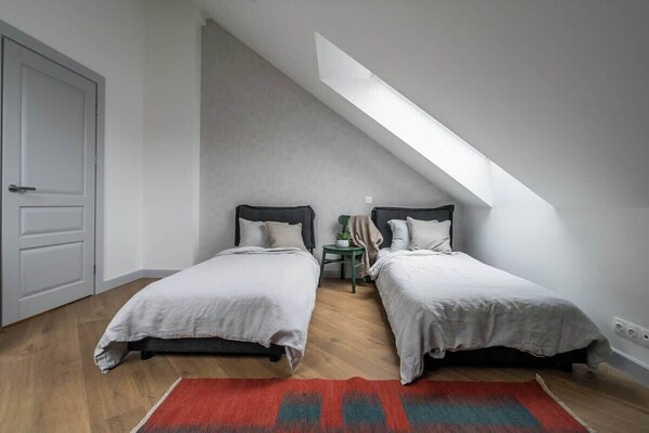 Ein Schlafzimmer mit zwei Betten, einem Dachfenster, einem roten Teppich und einem kleinen Tisch mit einer Pflanze.