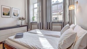 Habitación de hotel con dos camas, un ventanal con cortinas, una lámpara de pared y cuadros enmarcados.