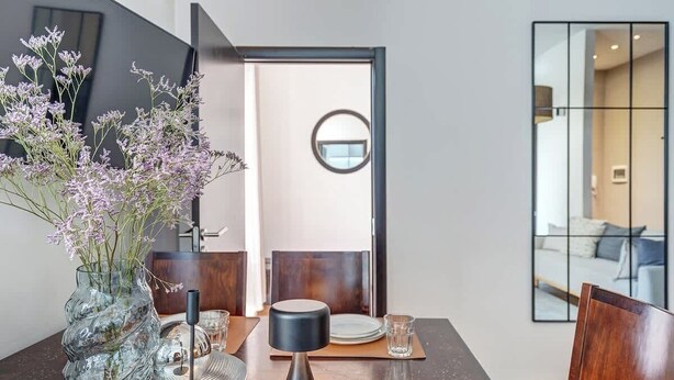 Un comedor moderno con un florero de cristal, un espejo redondo y una vajilla minimalista.