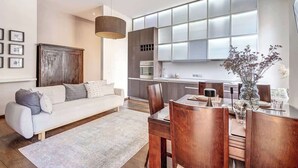 Una sala de estar moderna con un sofá, una mesa de comedor y sillas. Hay una zona de cocina con un ventanal y armarios.