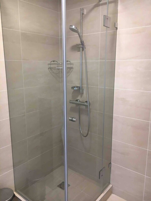 A glass-enclosed shower stall with a handheld showerhead, a wall-mounted faucet, and a small shelf. - Domillion 3bdr 2baths President Palace park. L419A (Vilnius)