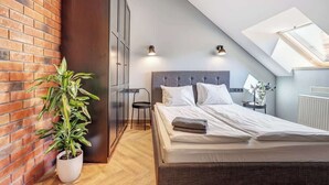 A bedroom with a sloped ceiling, a bed with white linens, a potted plant, a chair, and a radiator.