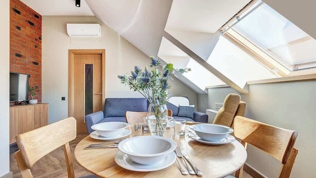 A modern dining area with a round wooden table set for four, a blue sofa, and a skylight above.