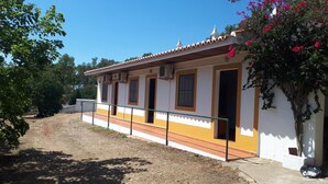 Un edificio con fachada blanca, detalles en naranja y techo de tejas. Tiene varias puertas y ventanas, y un pequeño porche.