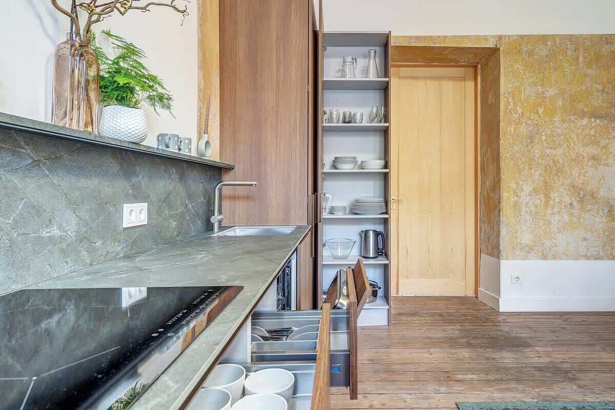 Une cuisine moderne dotée d’un four encastré, d’un meuble en bois et d’une étagère où sont rangés de la vaisselle.