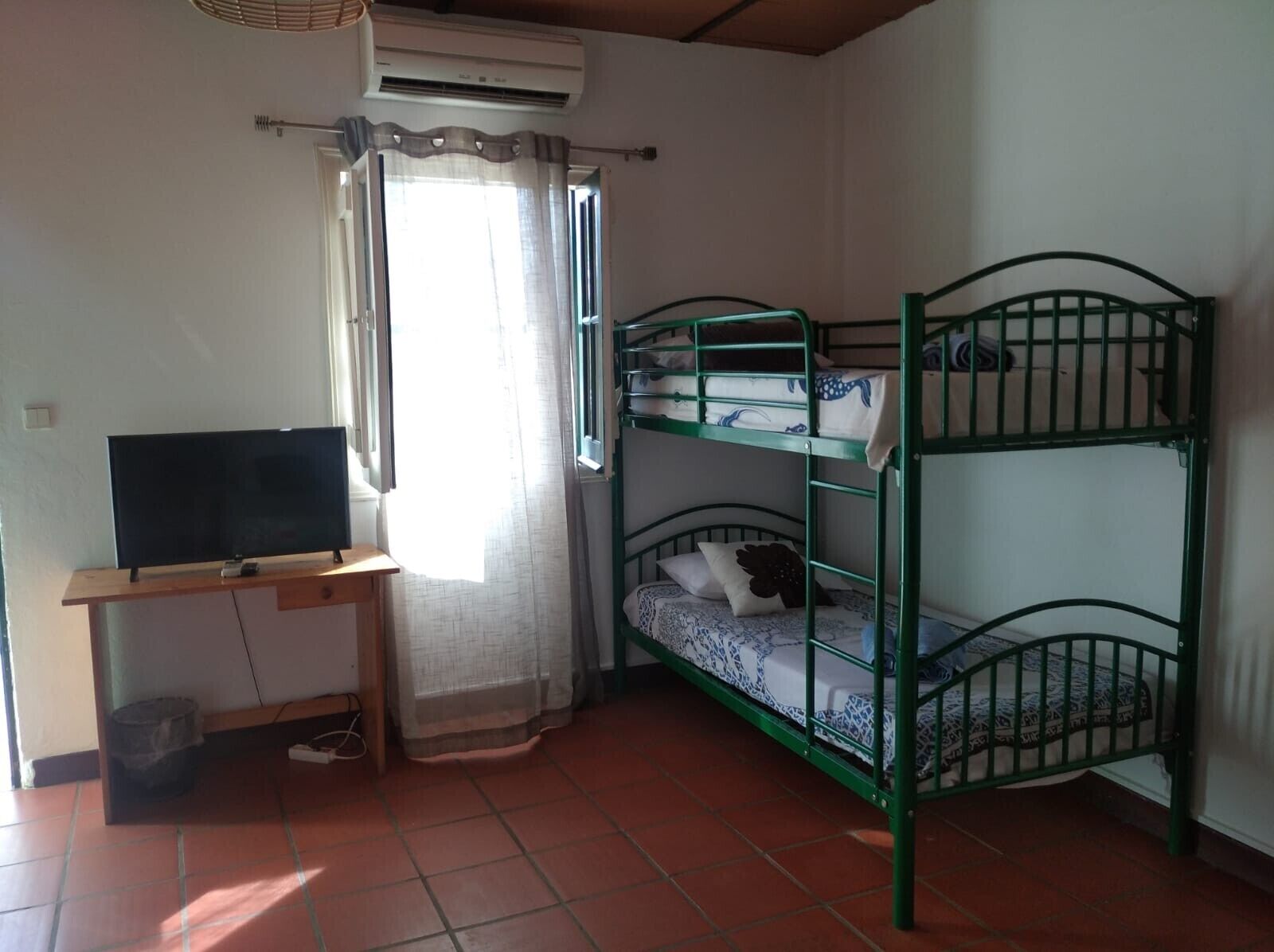 Une chambre avec un lit superposé, un bureau avec une télévision et une fenêtre avec des rideaux.