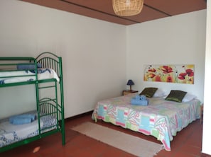 Een kamer met stapelbedden, een enkel bed met een kleurrijke quilt, een muurschildering, een lamp en een geweven plafondlamp.