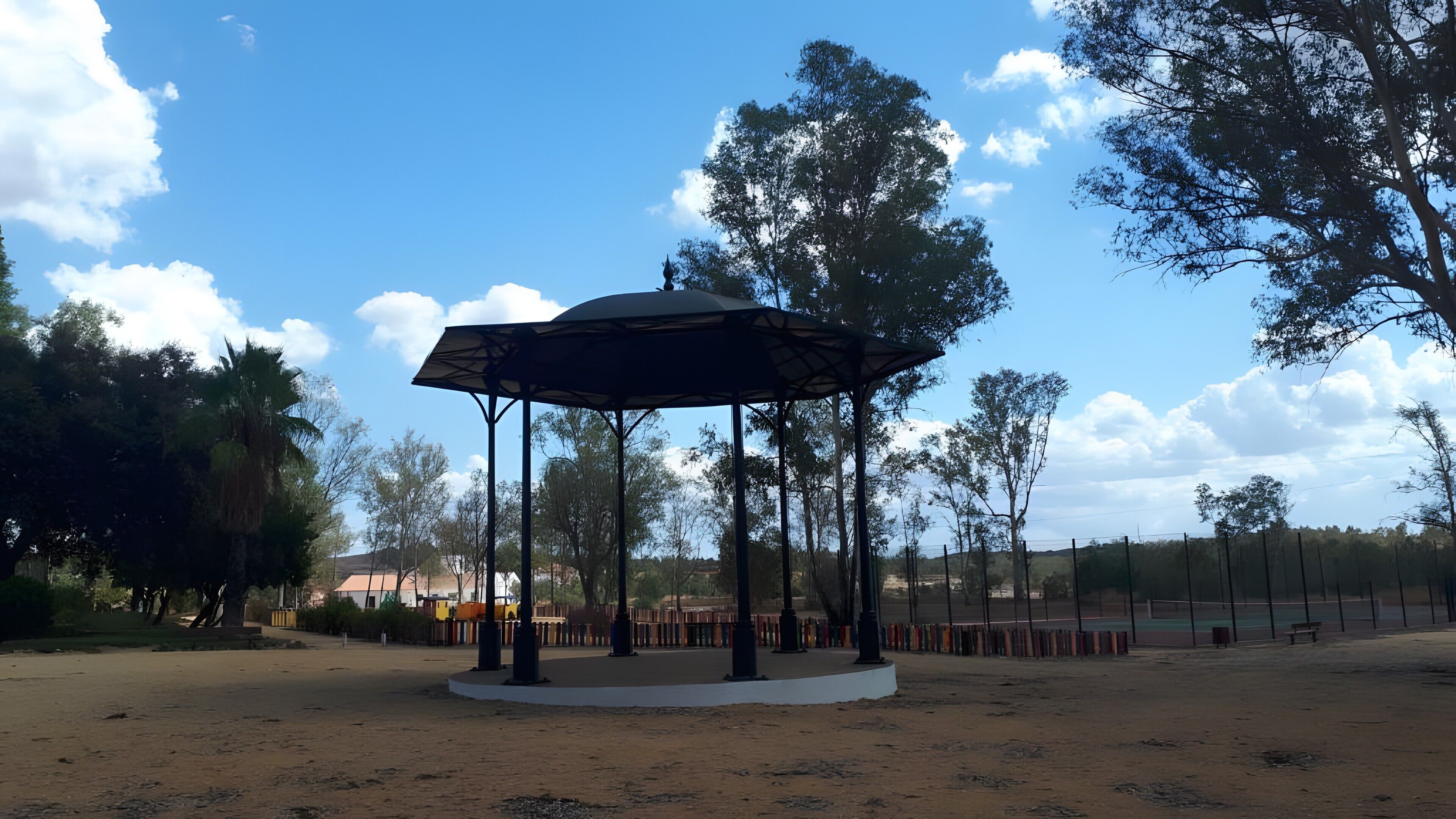 A gazebo in a park with trees and a fence in the background.
